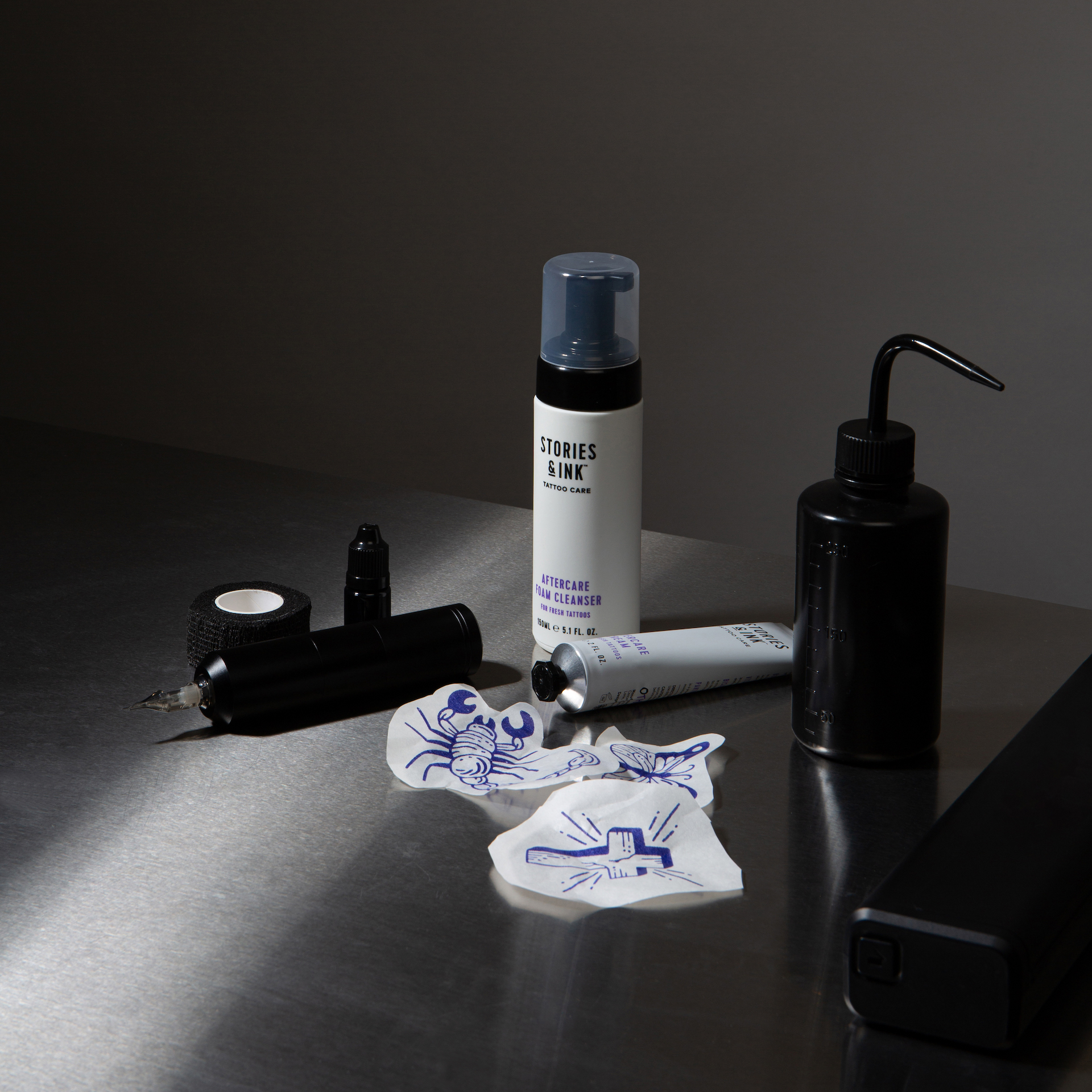 Stories & Ink aftercare foam cleanser and cream on a steel studio table with tattoo equipment